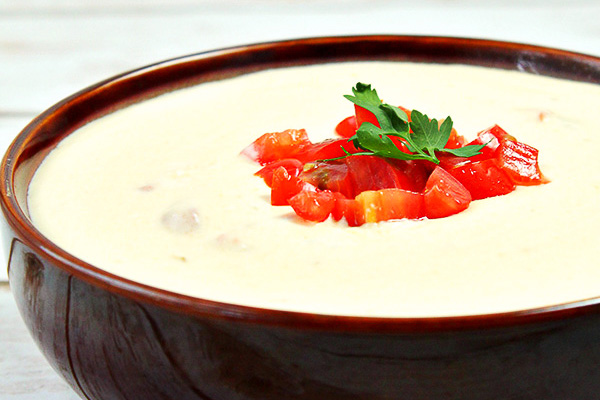 Homemade White Queso Dip in a brown bowl, surrounded by tortilla chips and topped with diced tomatoes