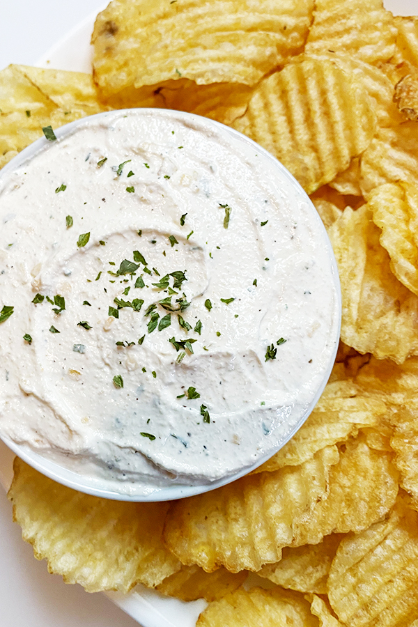 Bowl of Homemade Onion Chip Dip, surrounded by a plate of ripple potato chips on a white platter