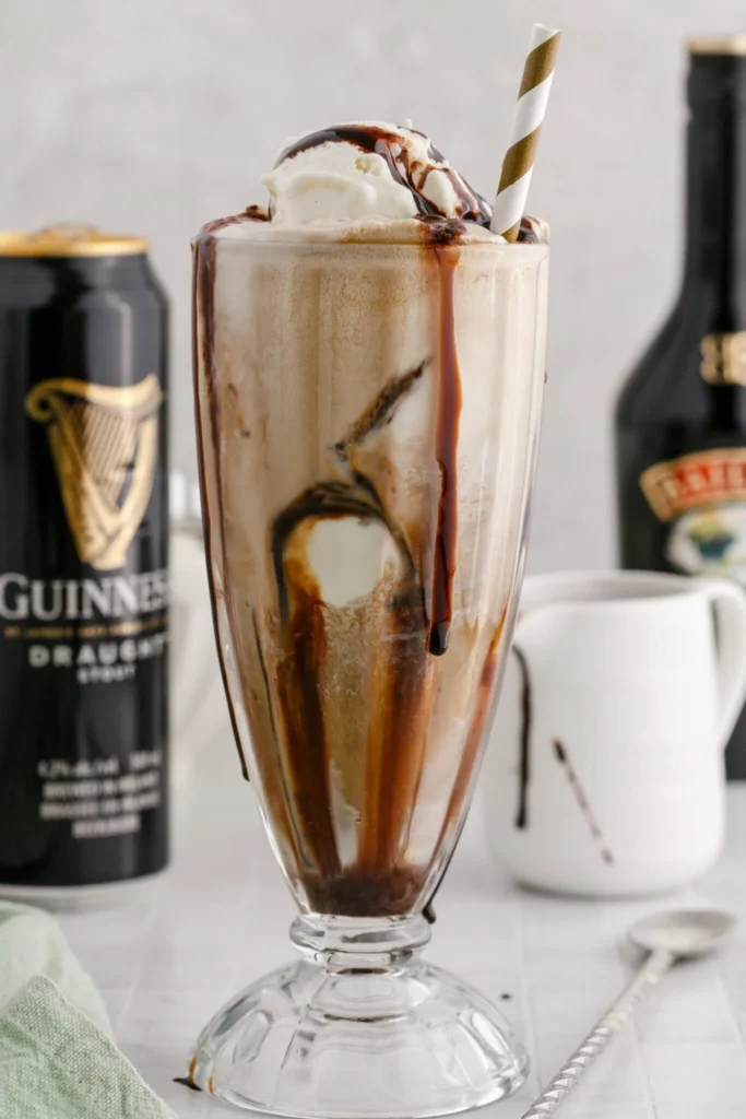 Baileys Irish Float served in a milkshake glass with a can of Guinness, a small white mug with chocolate, and a bottle of Baileys in the background.