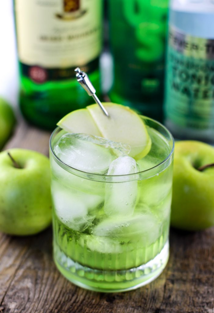 Irish Sour Apple Cocktail in a short glass cup with two green apples next to the glass.