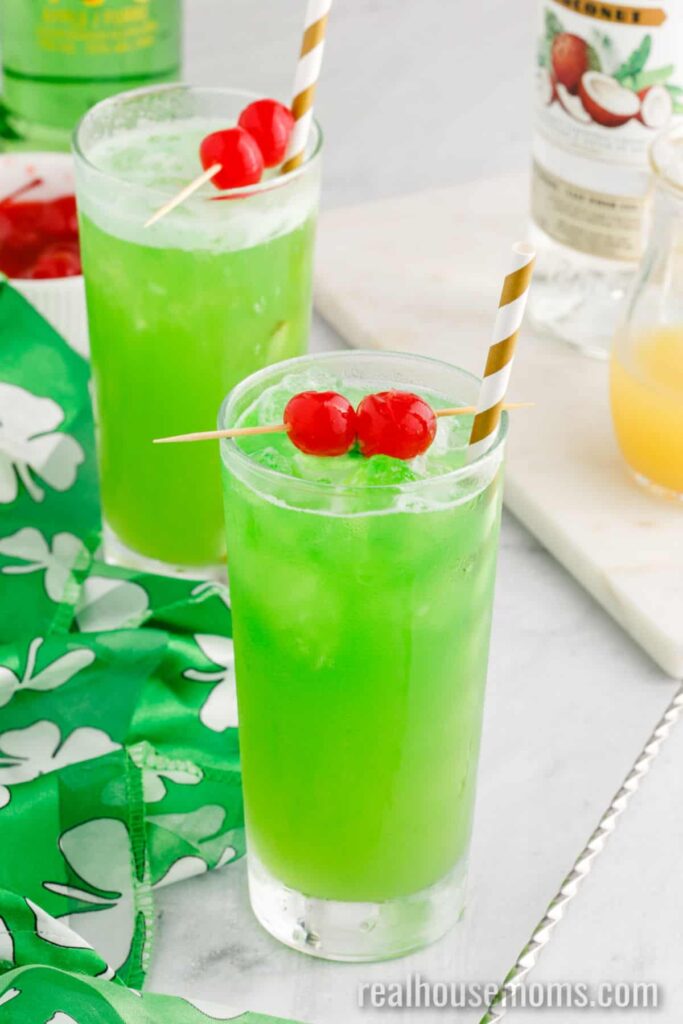 Two Pot of Gold Cocktail in tall glass cups with two cherries and a festive straw in each.