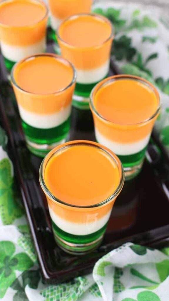 Six St. Patrick's Day Jello Shots on a black plate with a St. Patrick's Day fabric under it.