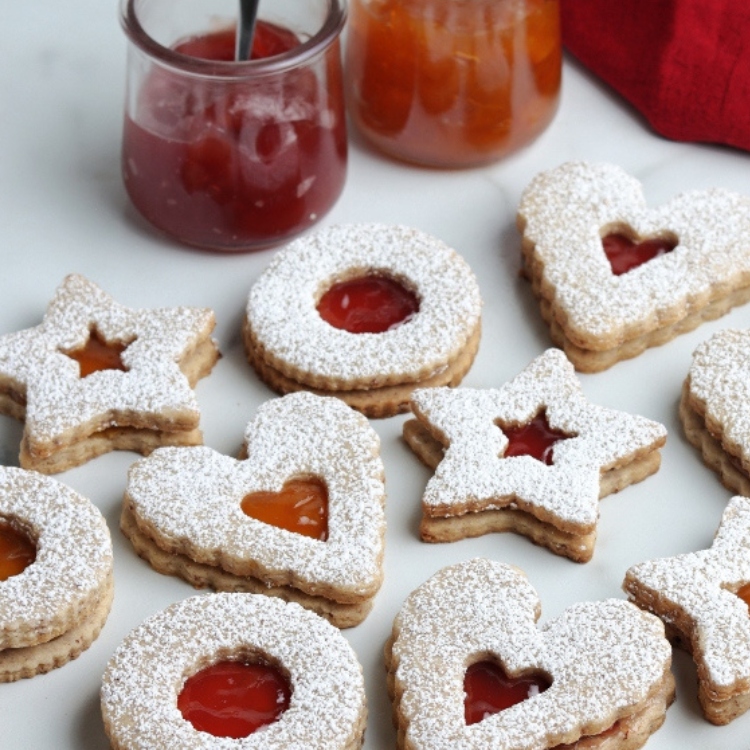 Linzer cookies on a white surface with jars of jams.